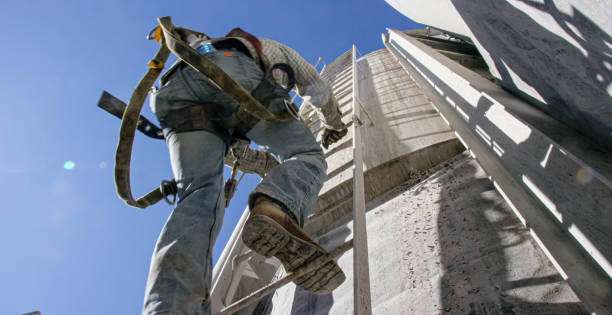 An Oilfield Worker Climbs a Ladder on the Side of a Mud Tank at an Oil and Gas Drilling Pad Site on a Sunny Morning